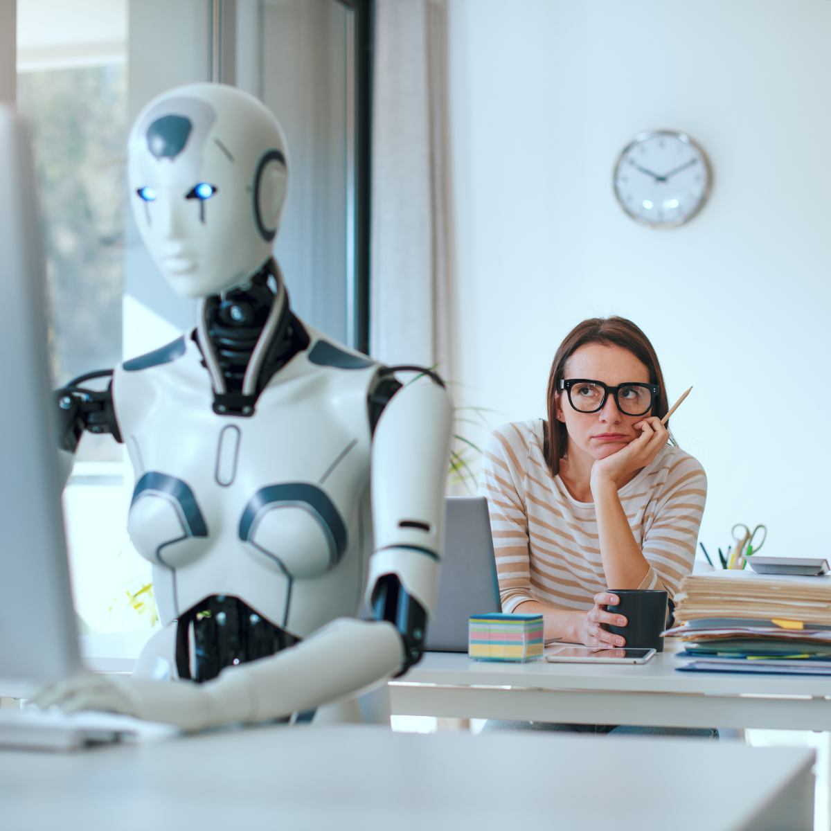 A woman at work sitting looking at a robot using a computer